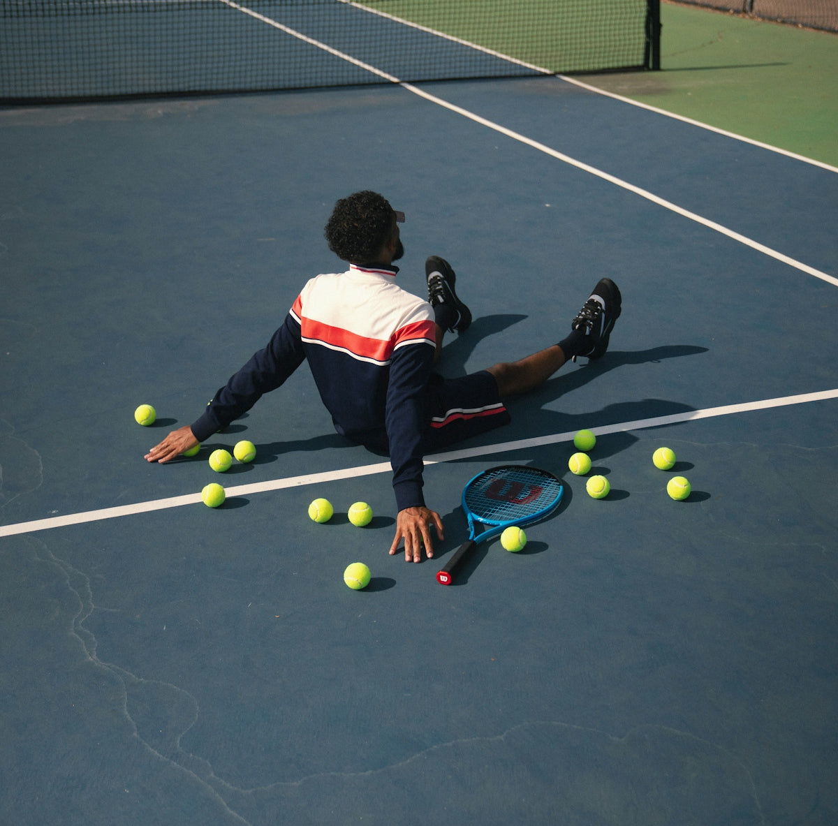 A man laying on a tennis court surrounded by tennis balls